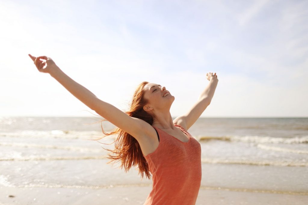 mulher feliz com os braços abertos na praia