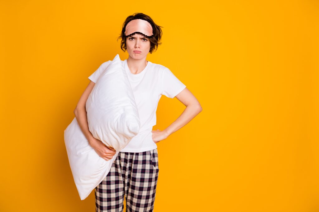 Mulher irritada de pijama segurando travesseiro